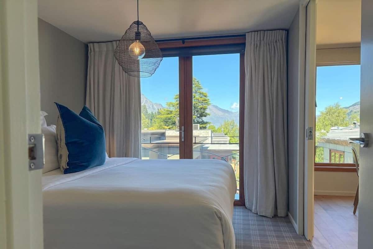 Habitación de hotel con una cama grande, una lámpara colgante y vistas de montañas a través de la ventana.