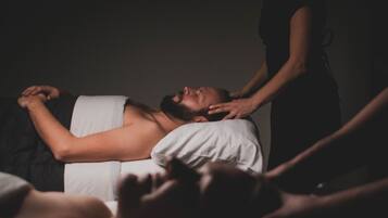 A massage therapy session in a dimly lit room with a person lying on a massage table receiving a back massage.