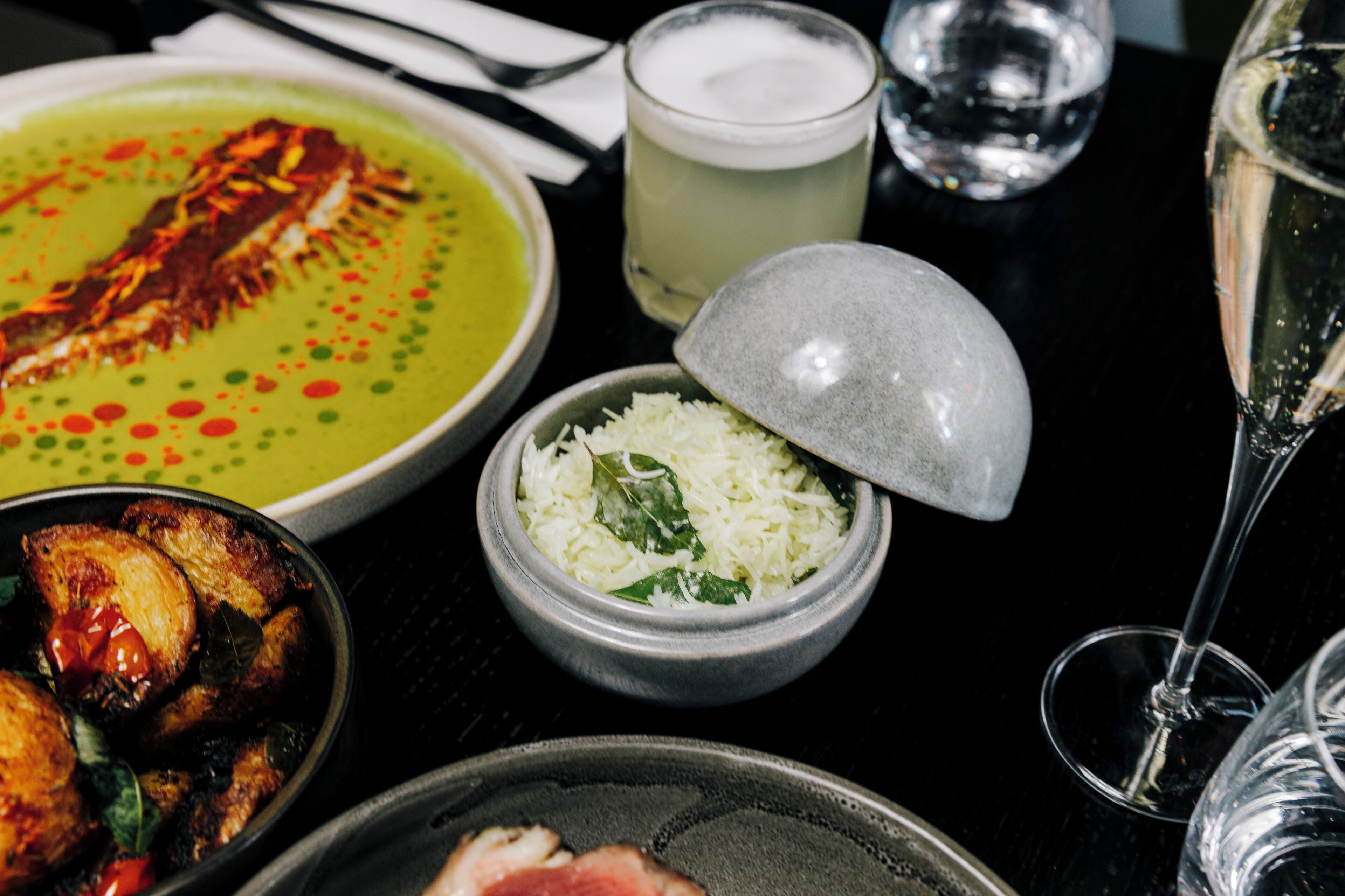 Una mesa con diversos platos, incluyendo un bol de arroz, un plato de pescado y un bol de sopa. También hay vasos y una taza sobre la mesa.