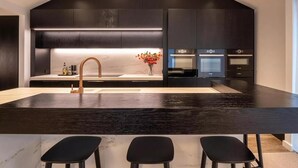 A modern kitchen with a dark countertop, a single gold faucet, and a vase with flowers. - The Spire Hotel Queenstown (Queenstown)