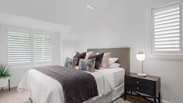 A bedroom with a bed, bedside table, lamp, and window blinds.