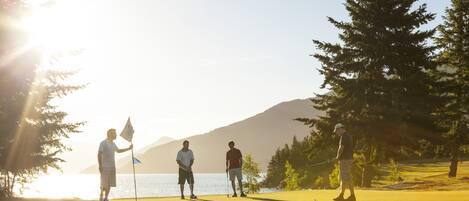 Un campo da golf con una bandierina, giocatori e una vista panoramica su un lago.
