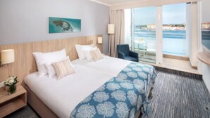 Habitación de hotel con una cama grande, vista al mar, balcón y un cuadro en la pared.