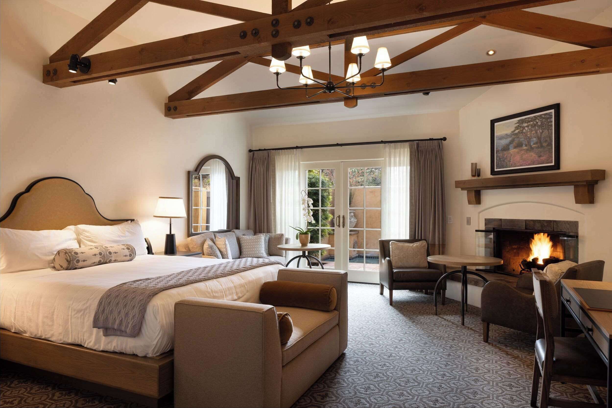 A bedroom with a large bed, a fireplace, a dining area, and a view of the outdoors.