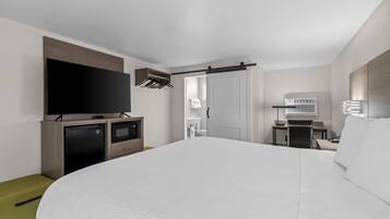 Habitación de hotel con una cama grande, televisor de pantalla plana, escritorio con silla, equipo de aire acondicionado y puerta corredera que da a un baño.