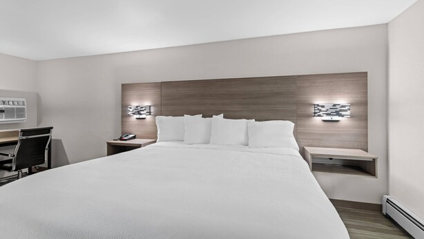 Moderni hotellihuone, jossa on suuri sänky, työpöytä ja tuoli. Huoneessa on kaksi yöpöytää, joissa on lamput.