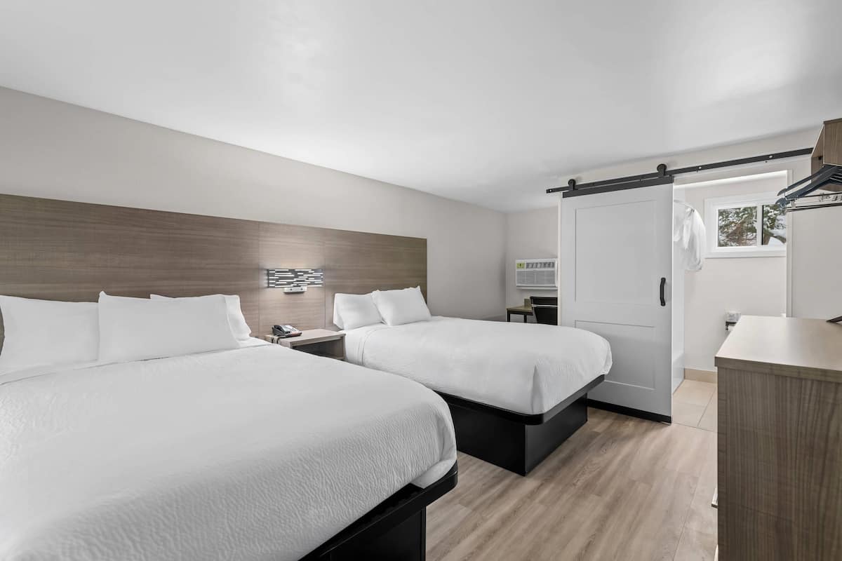 Une chambre d’hôtel moderne avec deux lits, une tête de lit en bois, un bureau et une porte coulissante donnant sur une autre pièce.