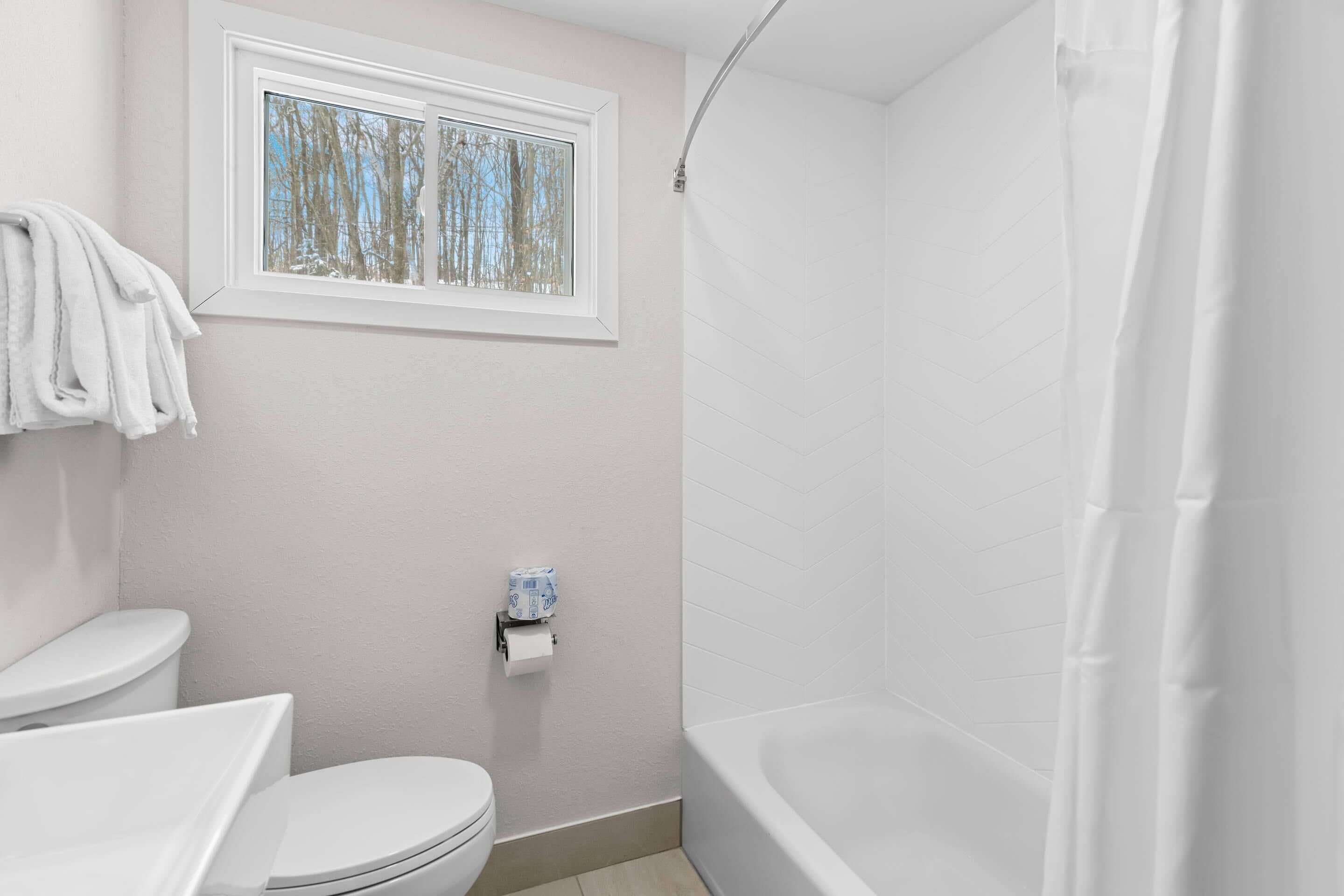 A bathroom with a toilet, a window, and a bathtub.
