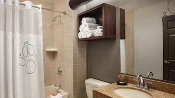 A bathroom with a shower curtain, a toilet, a sink with a mirror, and a towel shelf.