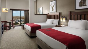 Habitación de hotel con dos camas, un escritorio, sillas y un ventanal con vistas.