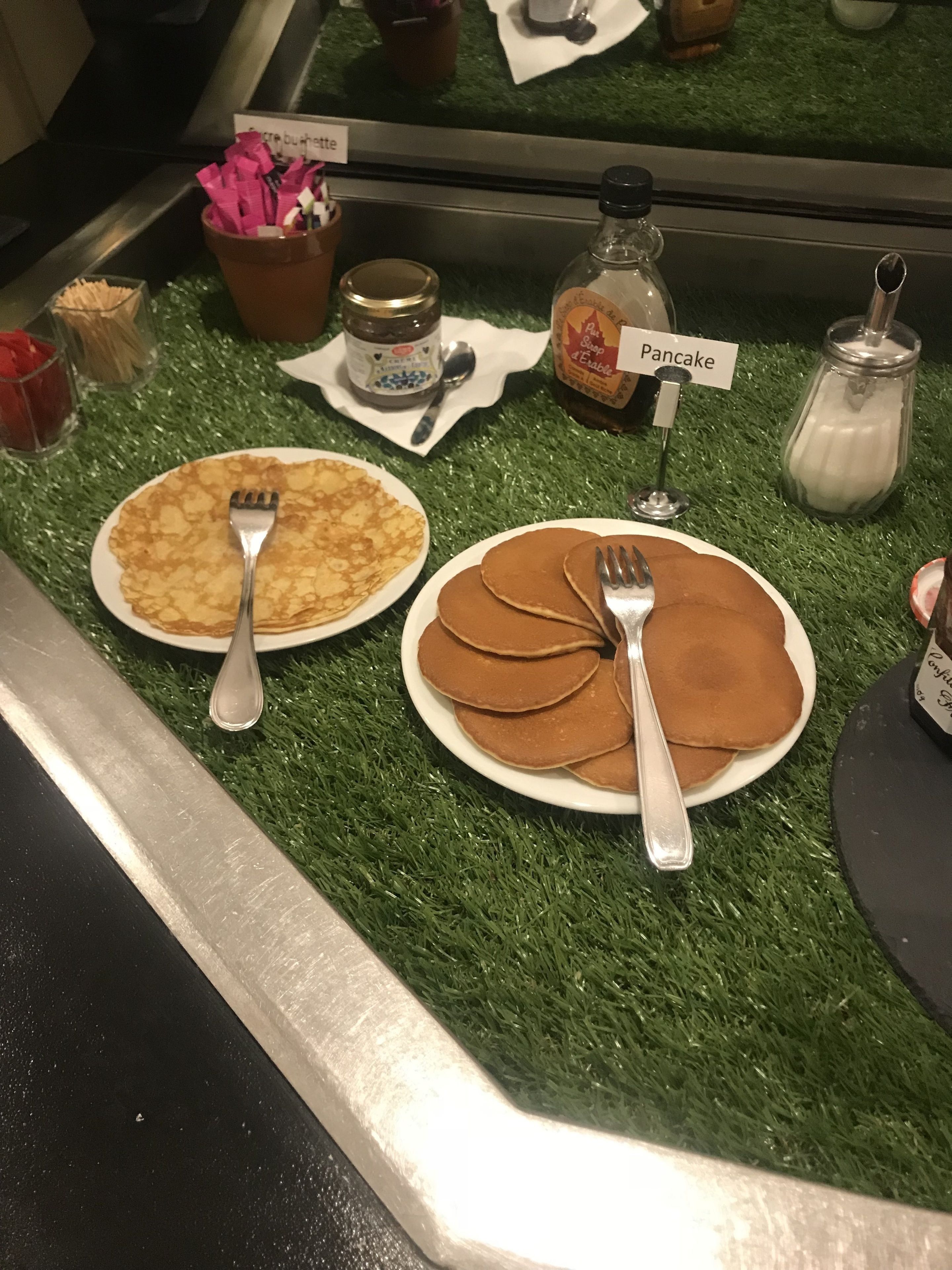 A breakfast setup with pancakes and a jar of syrup on a green artificial grass surface.