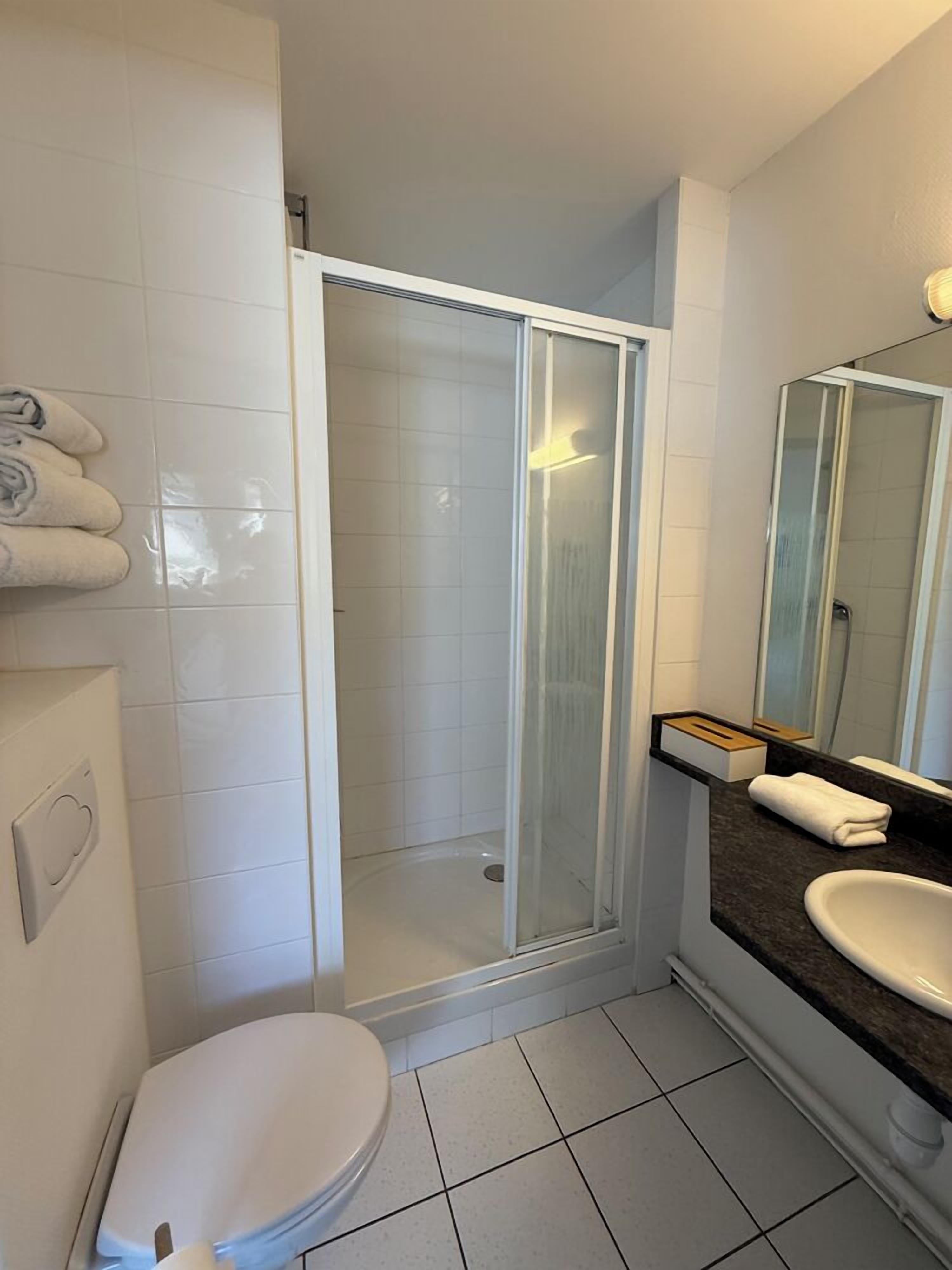 A bathroom with a toilet, a shower with a glass door, a sink with a mirror, and a towel rack.