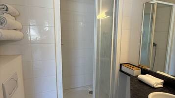 Un baño con inodoro, ducha con puerta de vidrio, lavamanos con espejo y un perchero para toallas.