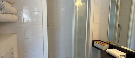 A bathroom with a toilet, a shower with a glass door, a sink with a mirror, and a towel rack.
