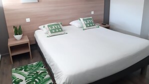 A neatly made bed with white bedding and two pillows, a small bedside table with a plant, and a wall-mounted artwork above the bed. - Brit Hotel Besançon L'Horloge (Besancon)