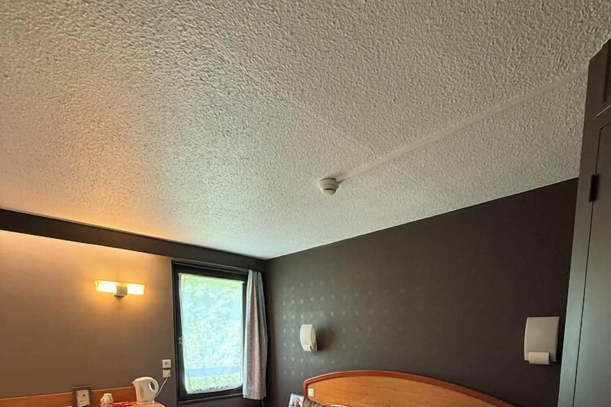 Habitación de hotel con una cama grande, un escritorio, una silla, una ventana con cortinas y un ventilador de techo.