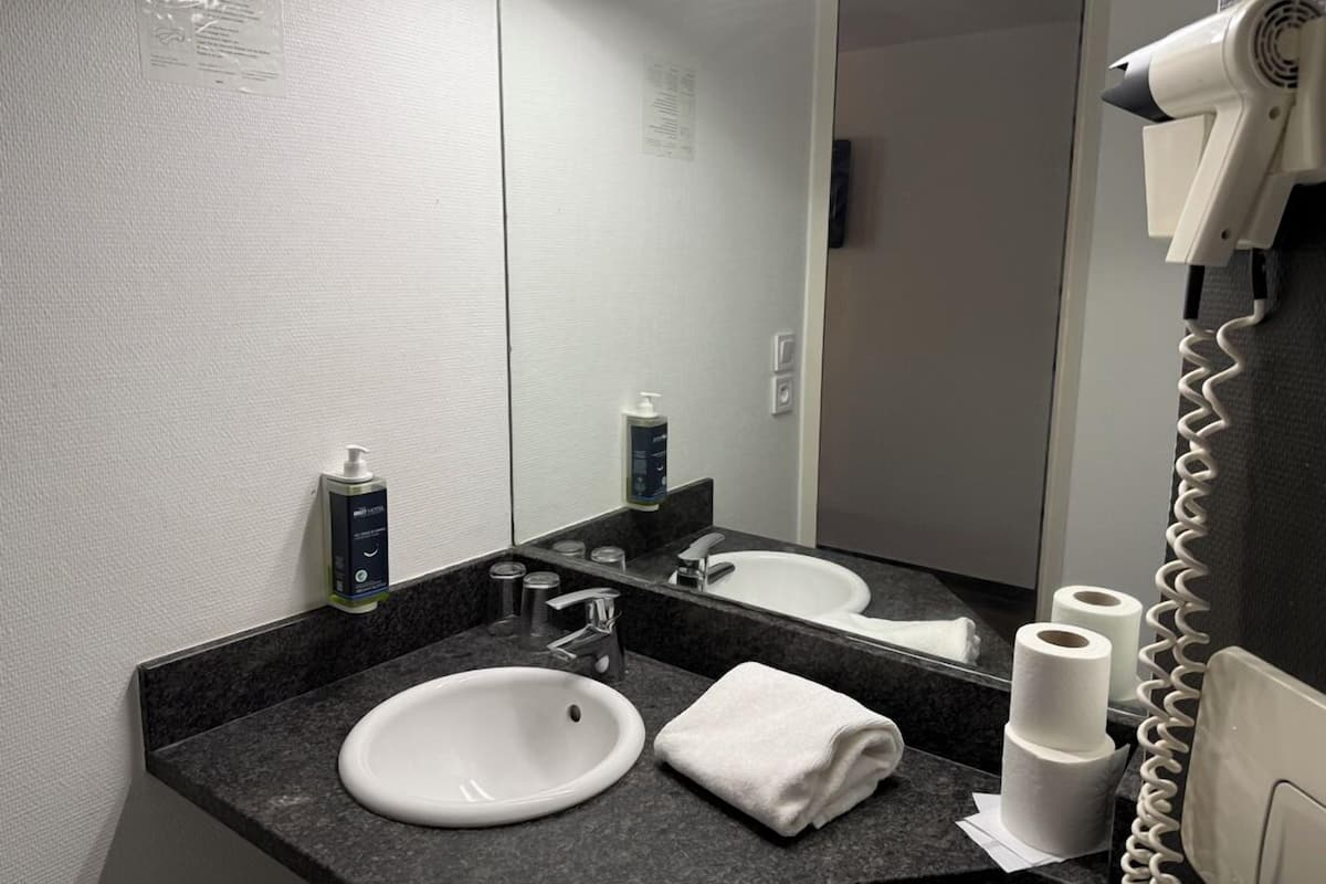 Un baño con un lavamanos blanco, un espejo, un secador de pelo y una toalla.