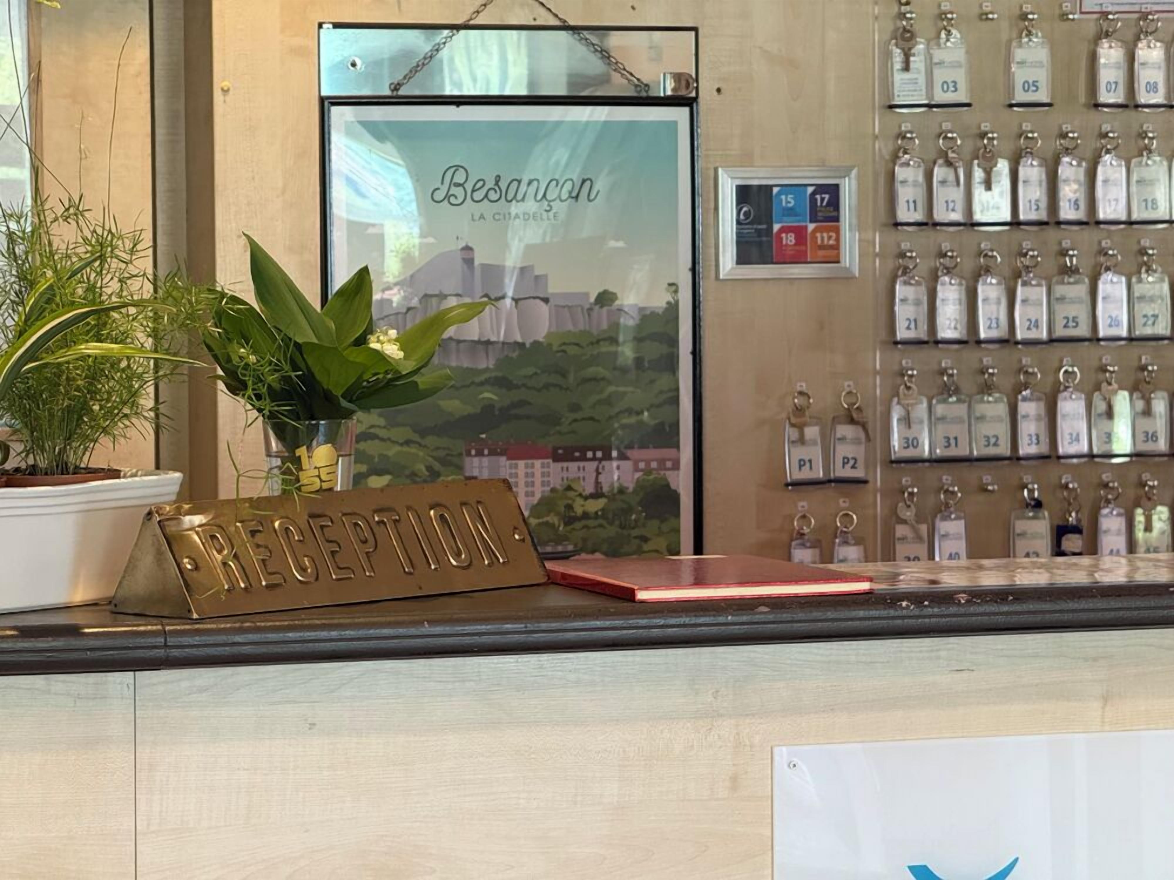 A reception desk with a 'RECEPTION' sign, a framed cityscape poster, and a wall of keychains.