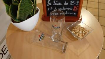 A round table with a potted plant, a glass of Heineken, a small bowl of peanuts, and a sign with a message in French.