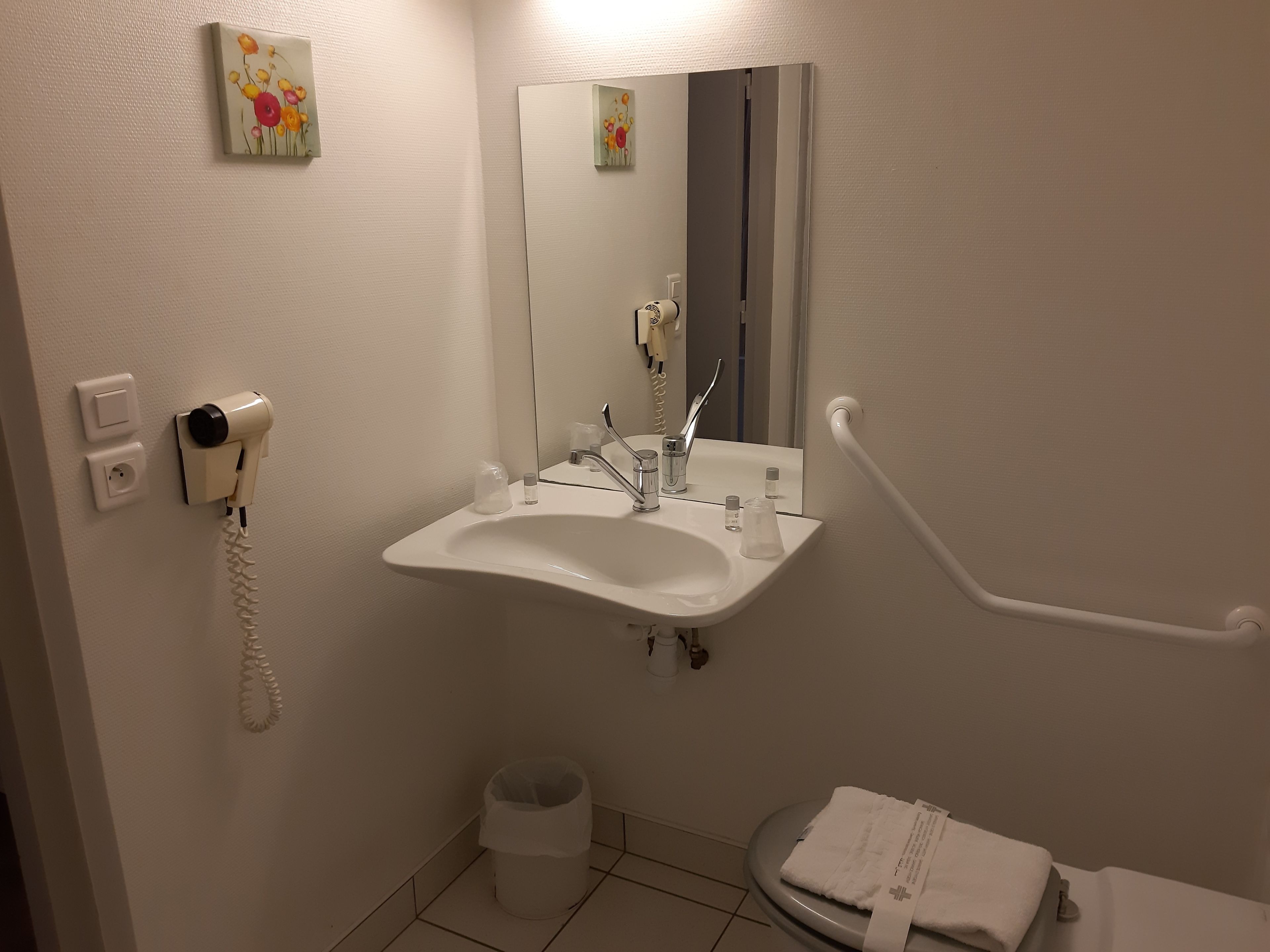 A bathroom with a sink, mirror, hand dryer, and a toilet.