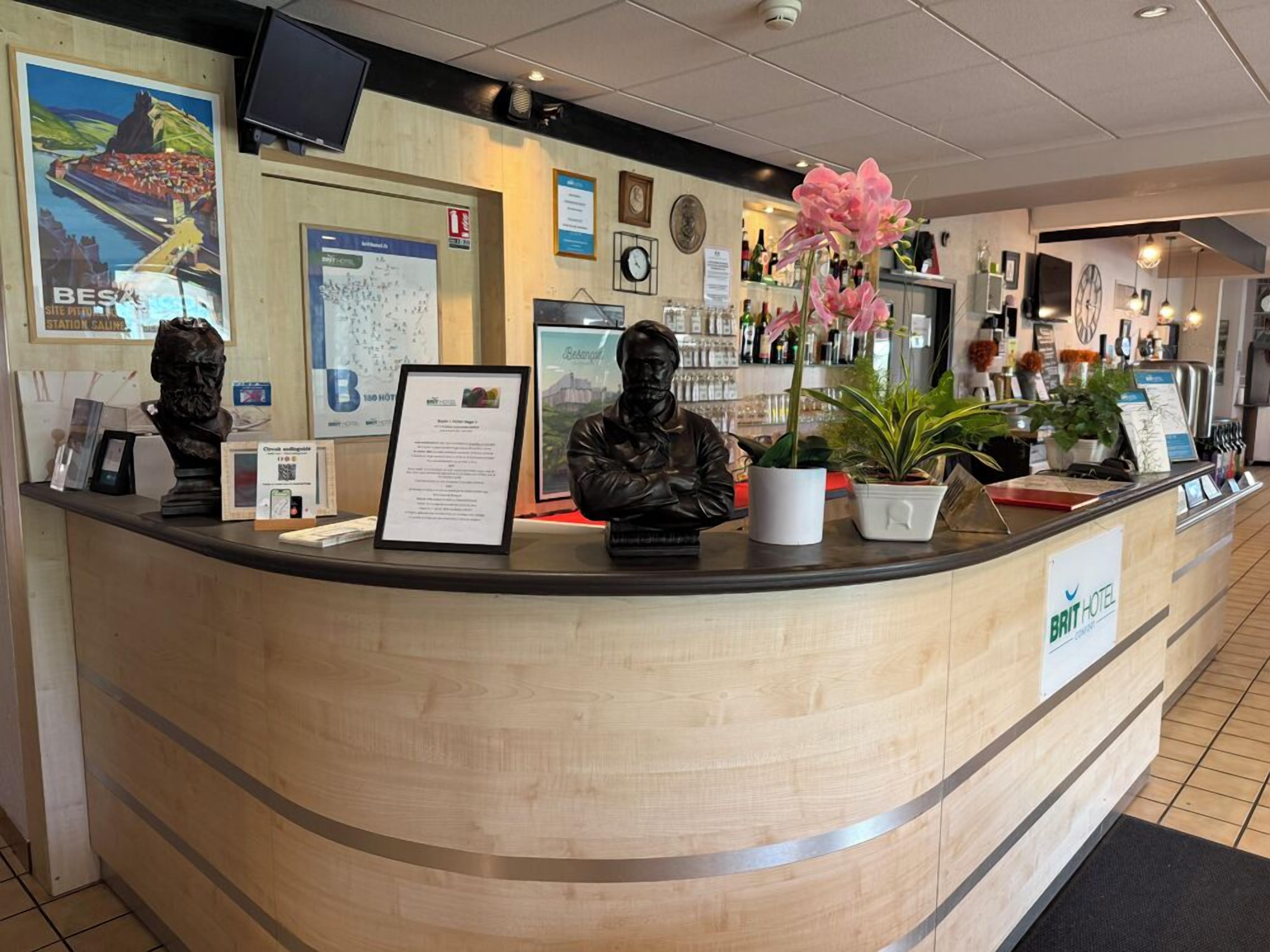 A hotel reception desk with busts, framed certificates, and a clock.