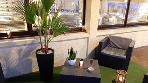 A seating area with a potted plant, a small table with a glass of drink, and a candle on a green mat. - Brit Hotel Besançon L'Horloge (Besancon)