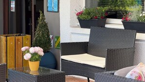 A seating area with wicker furniture and a glass table, surrounded by potted plants and a small tree. - Brit Hotel Besançon L'Horloge (Besancon)