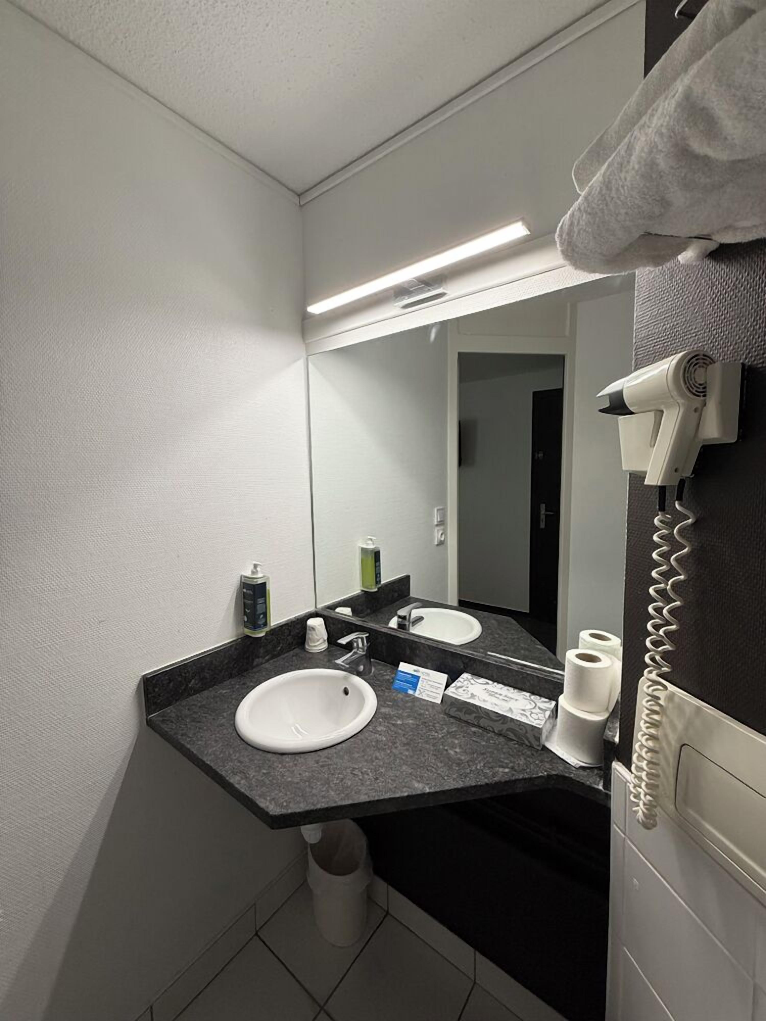 A hotel bathroom with a white sink, a mirror, a hairdryer, and a towel rack.