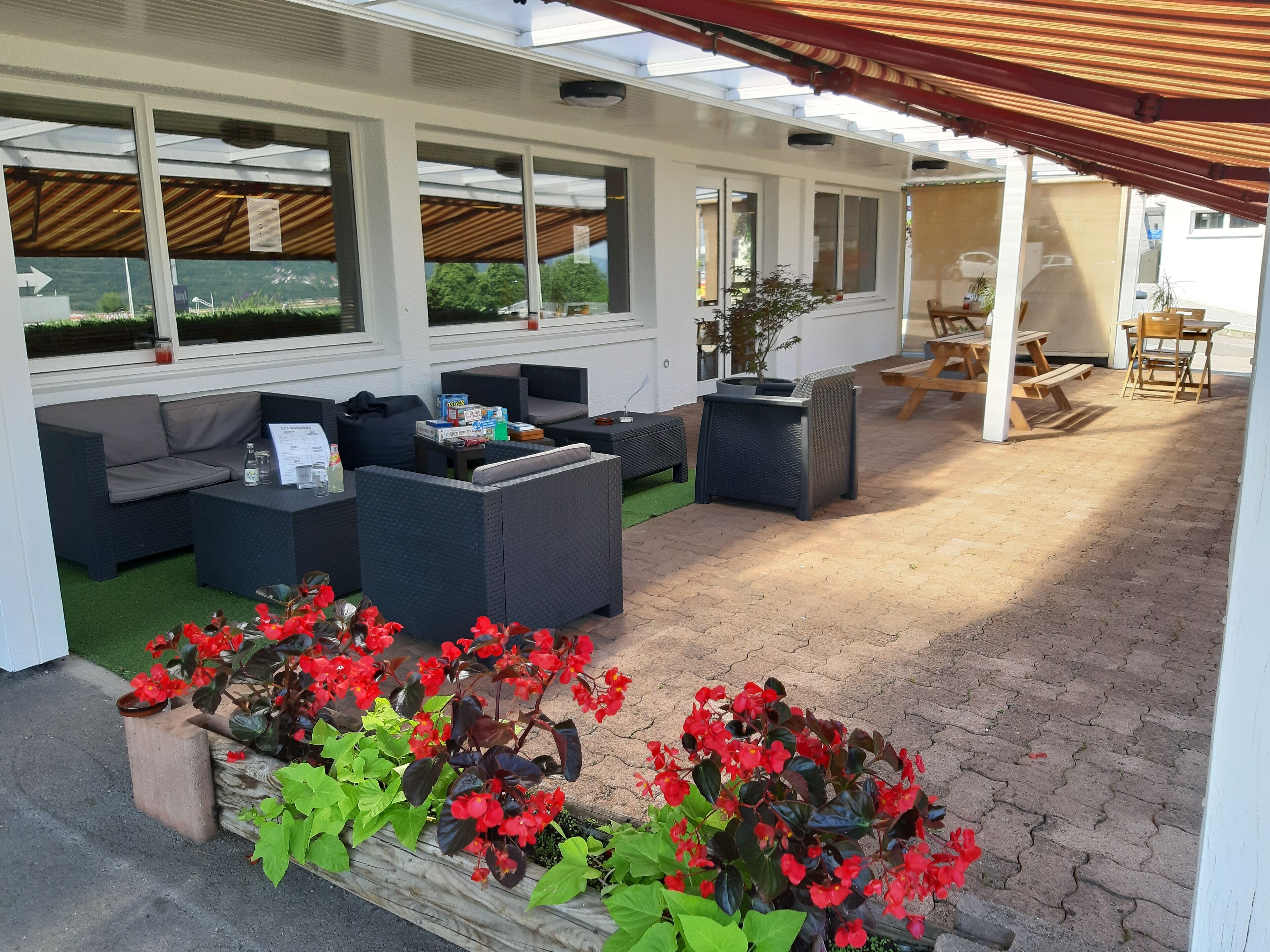 An outdoor patio with seating, a table, and planters with red flowers.
