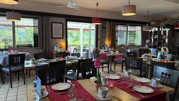 Een restaurant met meerdere tafels, stoelen en hangende lampen.