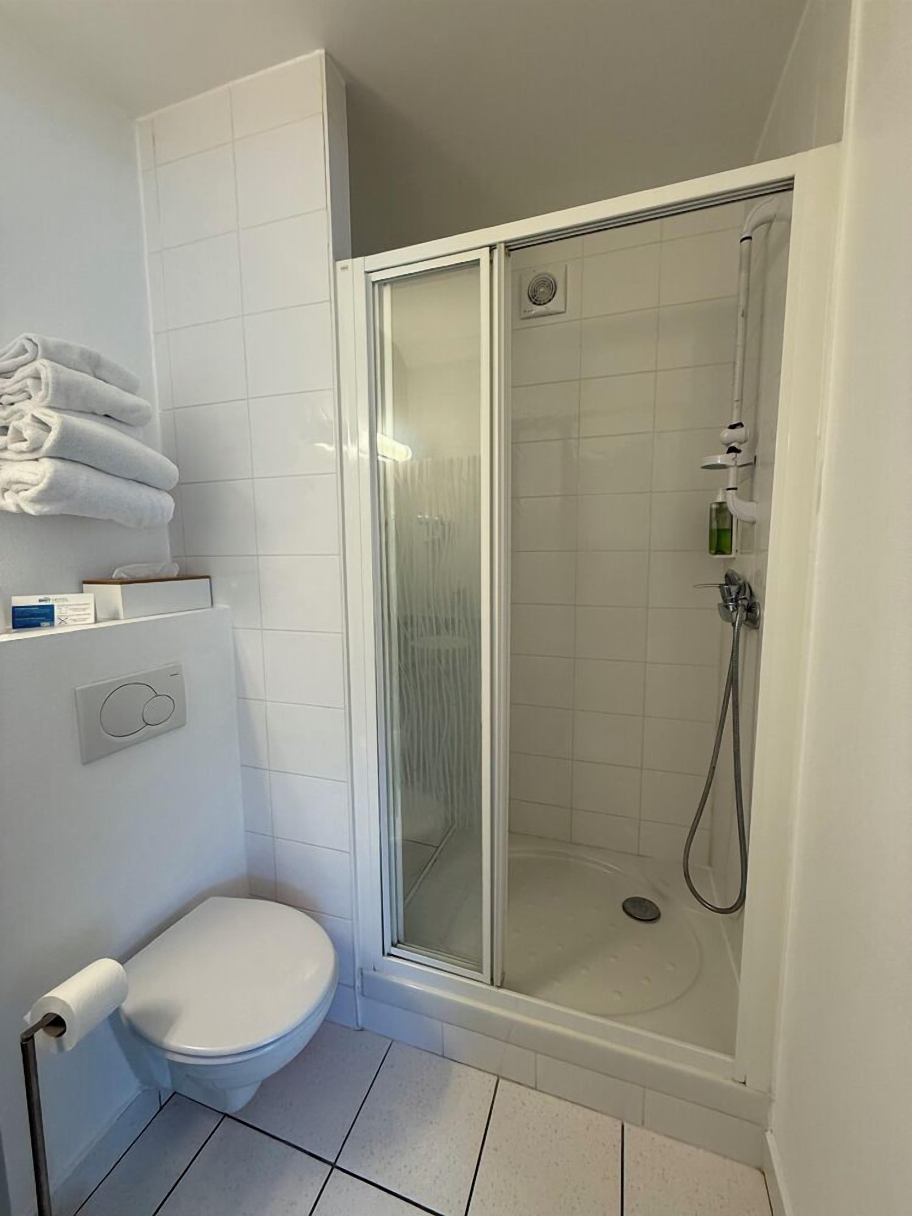 A bathroom with a toilet, a glass-enclosed shower, and a towel rack with folded towels.