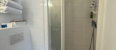 A bathroom with a toilet, a glass-enclosed shower, and a towel rack with folded towels.
