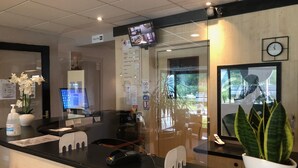 A hotel reception area with a computer monitor, a clock, and a potted plant. - Brit Hotel Besançon L'Horloge (Besancon)