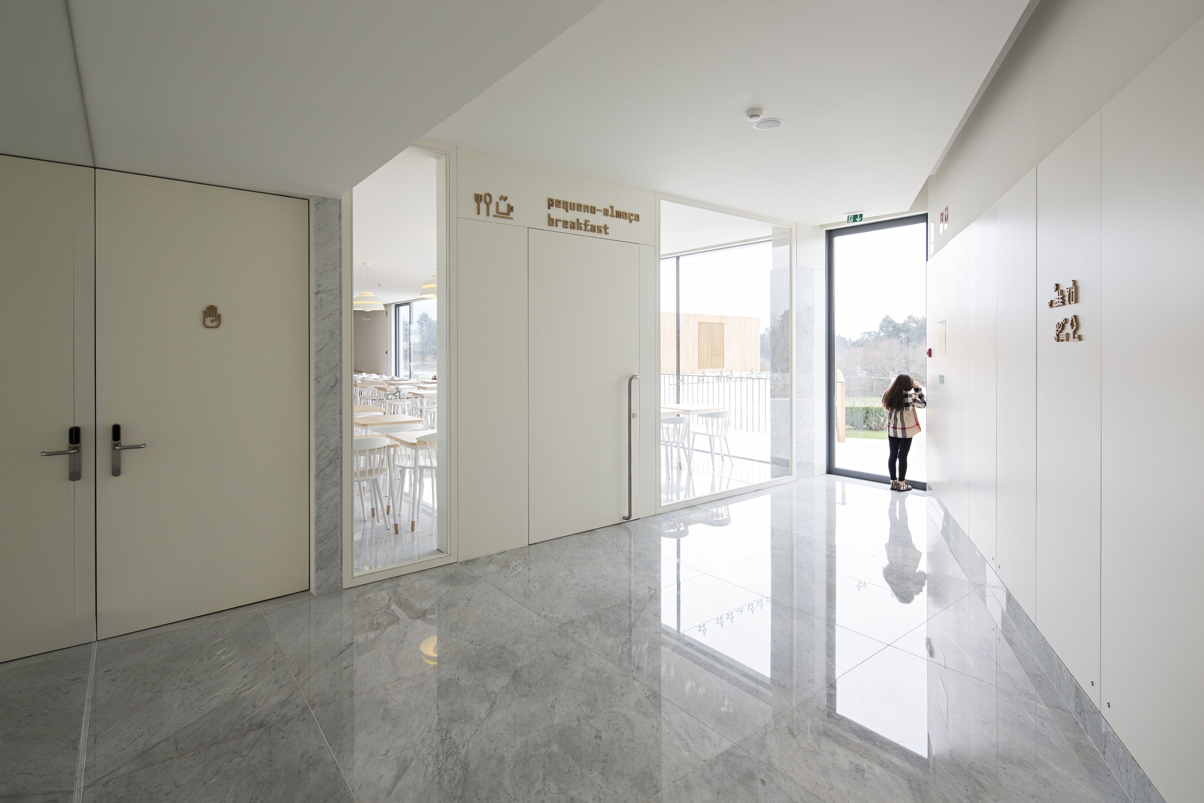 Un pasillo moderno de hotel con piso de mármol pulido, un cartel de desayuno y vistas al exterior.