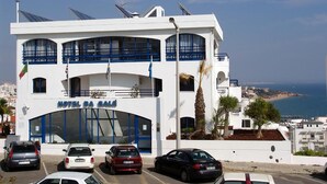 Un hotel con una entrada destacada, varios balcones y vista al mar.