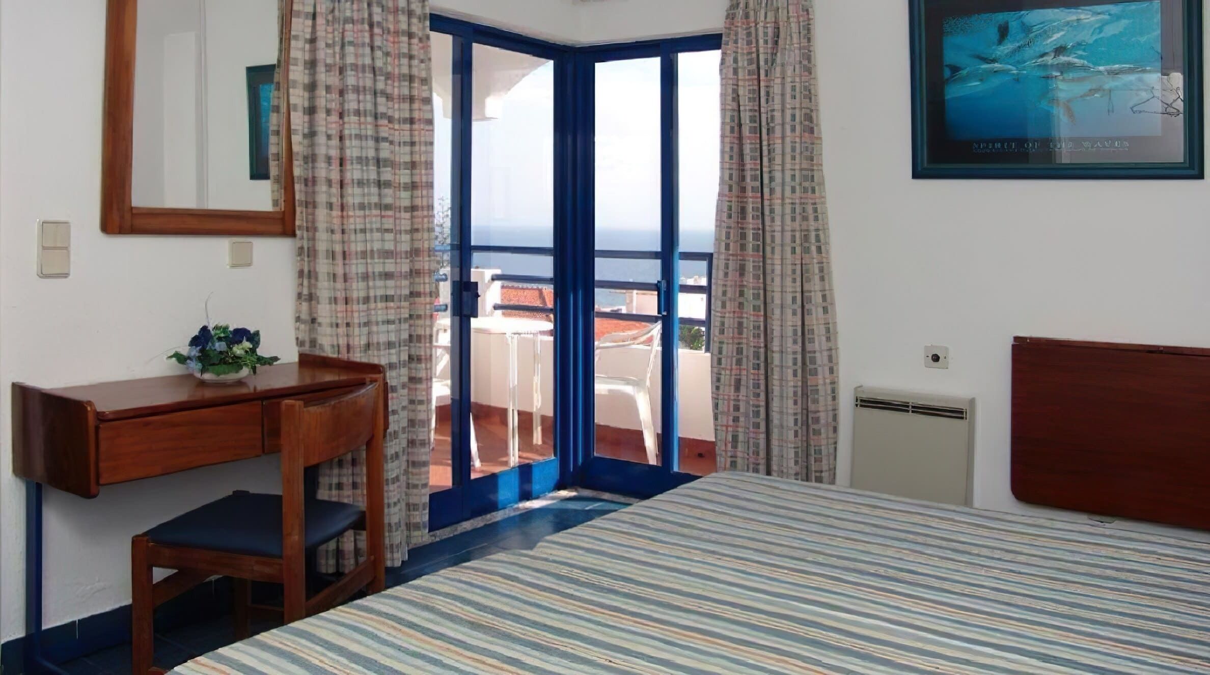 Une chambre d’hôtel avec un lit, un bureau, une chaise, une fenêtre avec des rideaux et un tableau encadré au mur.