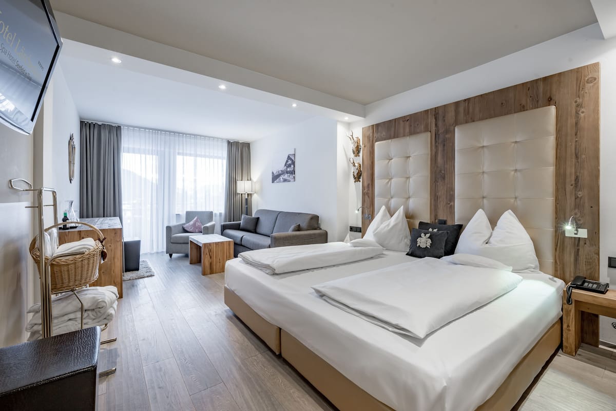 A modern hotel room with a large bed, a sofa, a desk, and a TV.