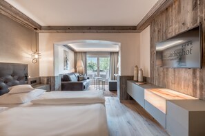 A modern hotel room with a large bed, a sofa, a desk, and a TV mounted on the wall. - Natur & Spa Hotel Lärchenhof (Seefeld in Tirol)