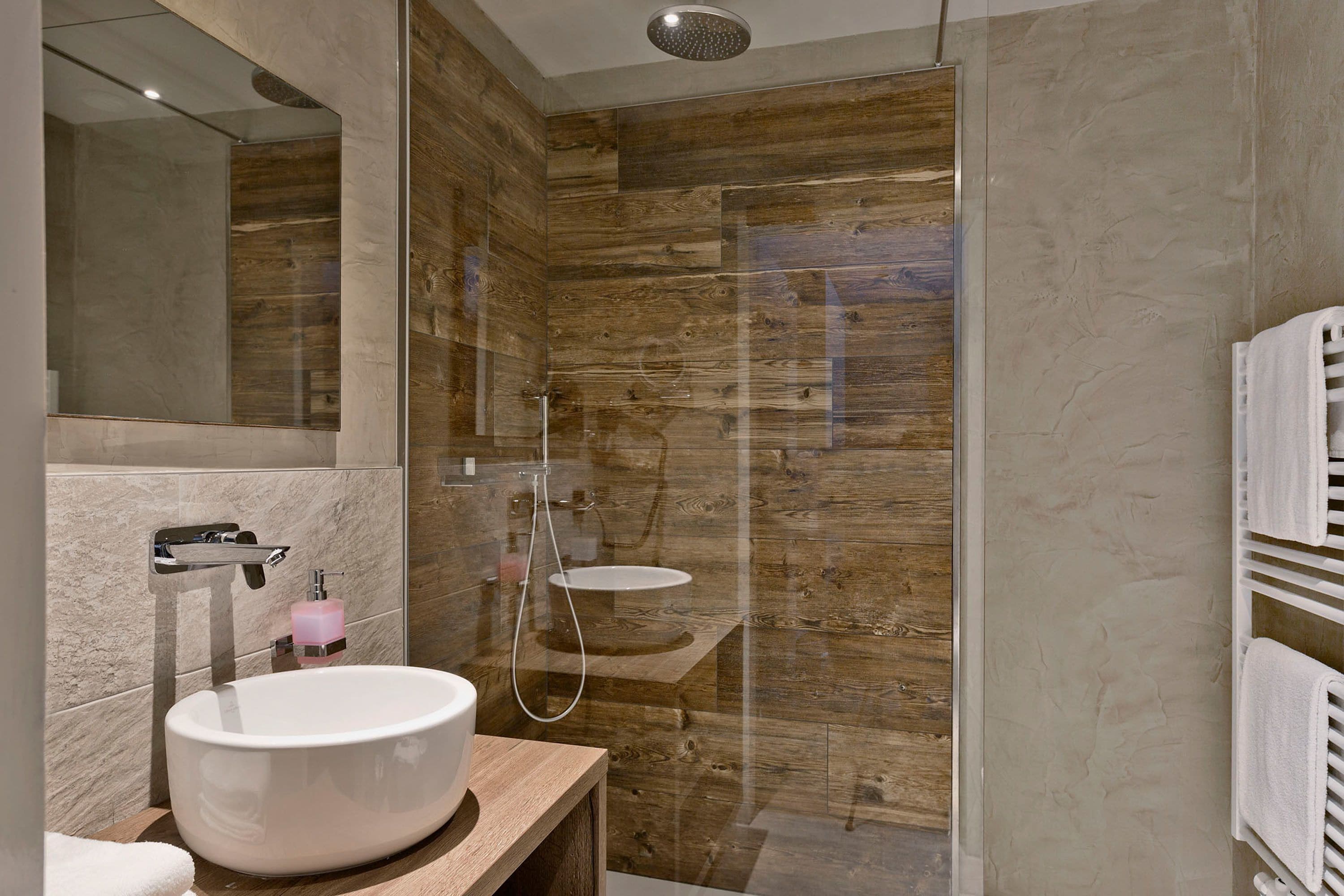 Un baño moderno con un lavabo grande de color blanco, cabina de ducha con mampara de vidrio y un panel de pared de madera.