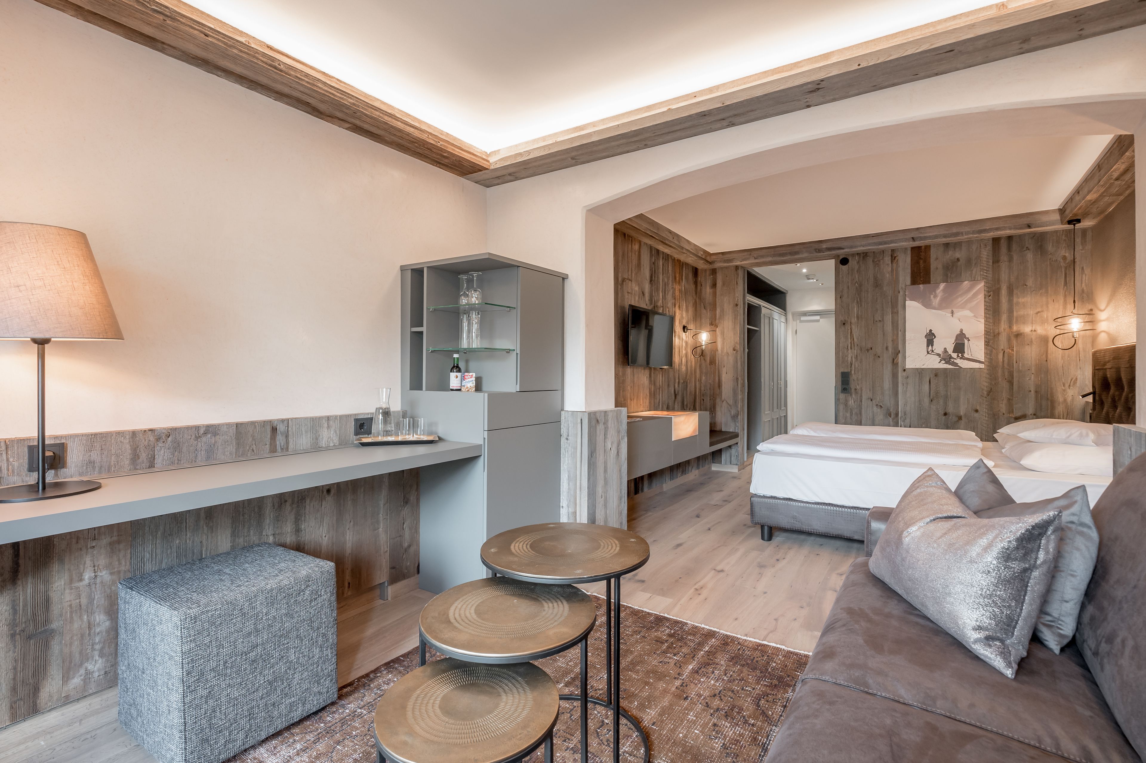 Una habitación de hotel moderna con techo de madera, un sofá, una mesita y una cama.
