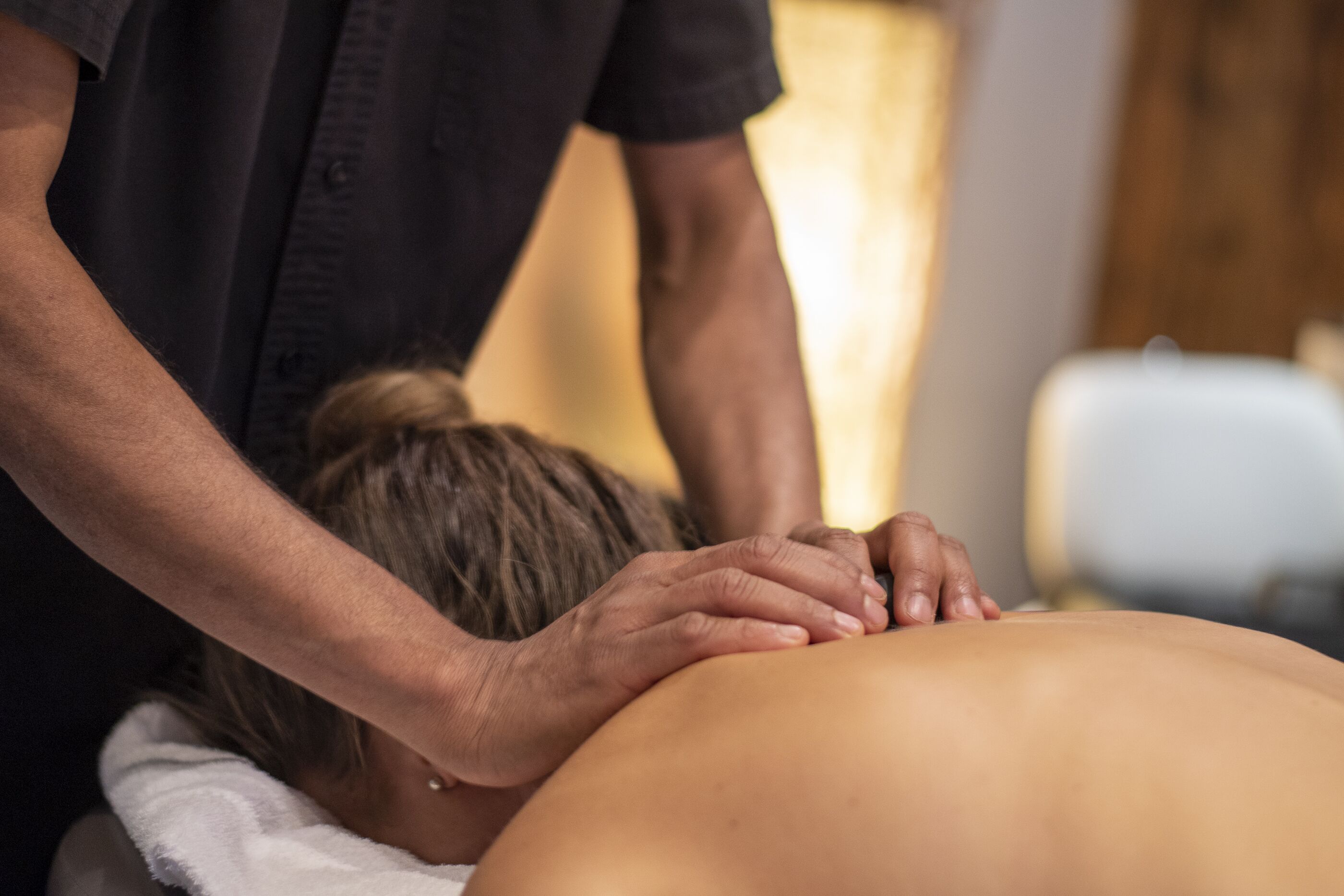 A person receiving a massage in a room with a wooden floor and a white chair.