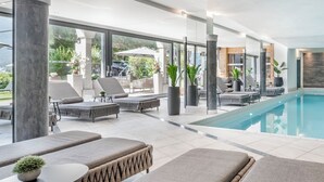 A modern indoor pool area with lounge seating, large windows, and a clear view of the outdoors. - Natur & Spa Hotel Lärchenhof (Seefeld in Tirol)