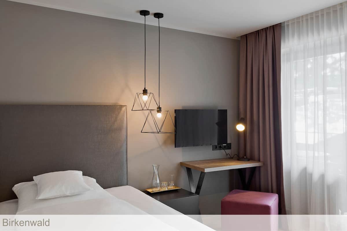 A modern hotel room with a large bed, a desk with a flat-screen TV, and a pendant light fixture.