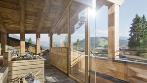 A wooden deck with a view of mountains, a grill, and a metal bowl on a table. - Natur & Spa Hotel Lärchenhof (Seefeld in Tirol)