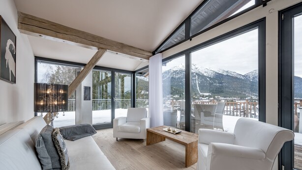 A modern living room with a large window, white furniture, and a wooden coffee table. - Natur & Spa Hotel Lärchenhof (Seefeld in Tirol)