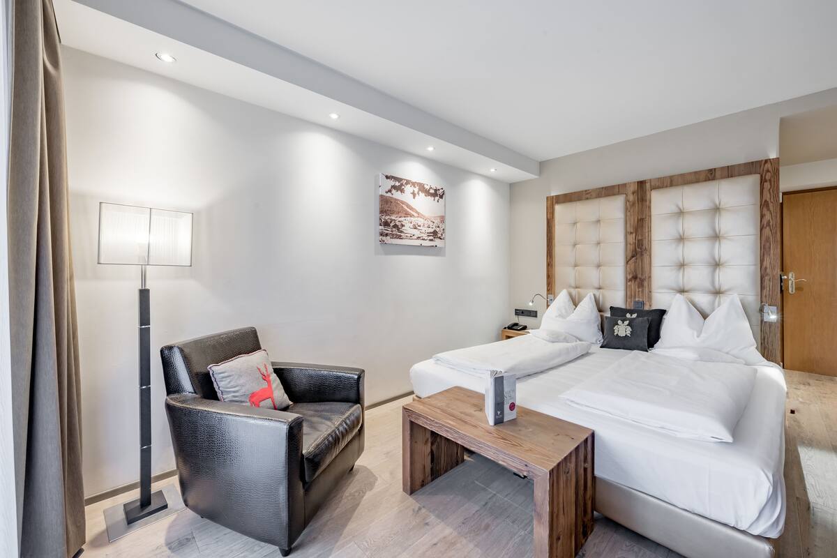 A modern hotel room with a bed, a chair, a bedside table, a lamp, and a picture on the wall.