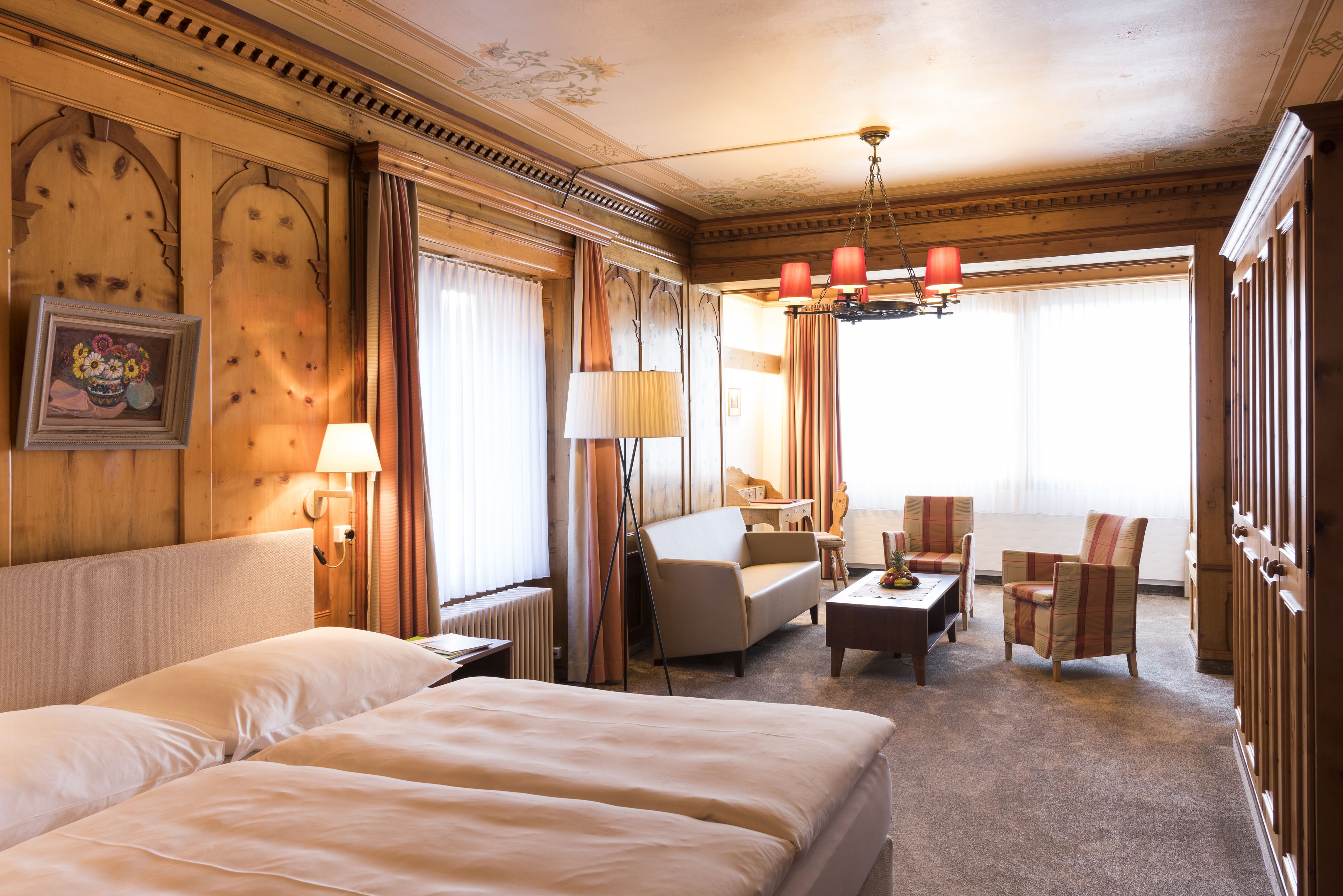 Habitación de hotel con una cama grande, un sofá, dos sillones, un escritorio y una araña.