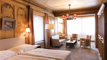 Une chambre d’hôtel avec un grand lit, un canapé, deux fauteuils, un bureau et un lustre.