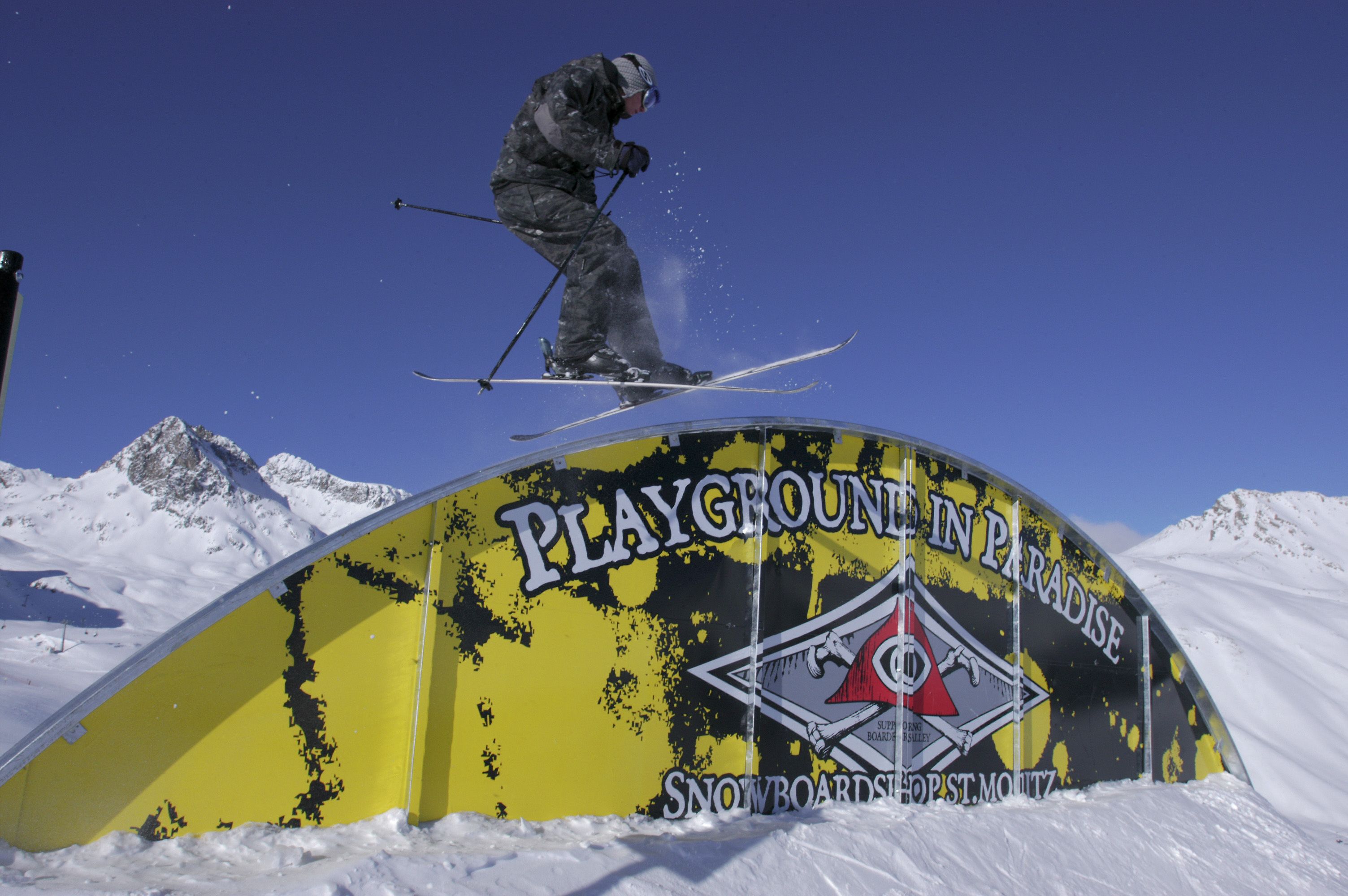 A ski jump ramp with a sign that reads "Playground in Paradise Snowboardshop St. Moritz."