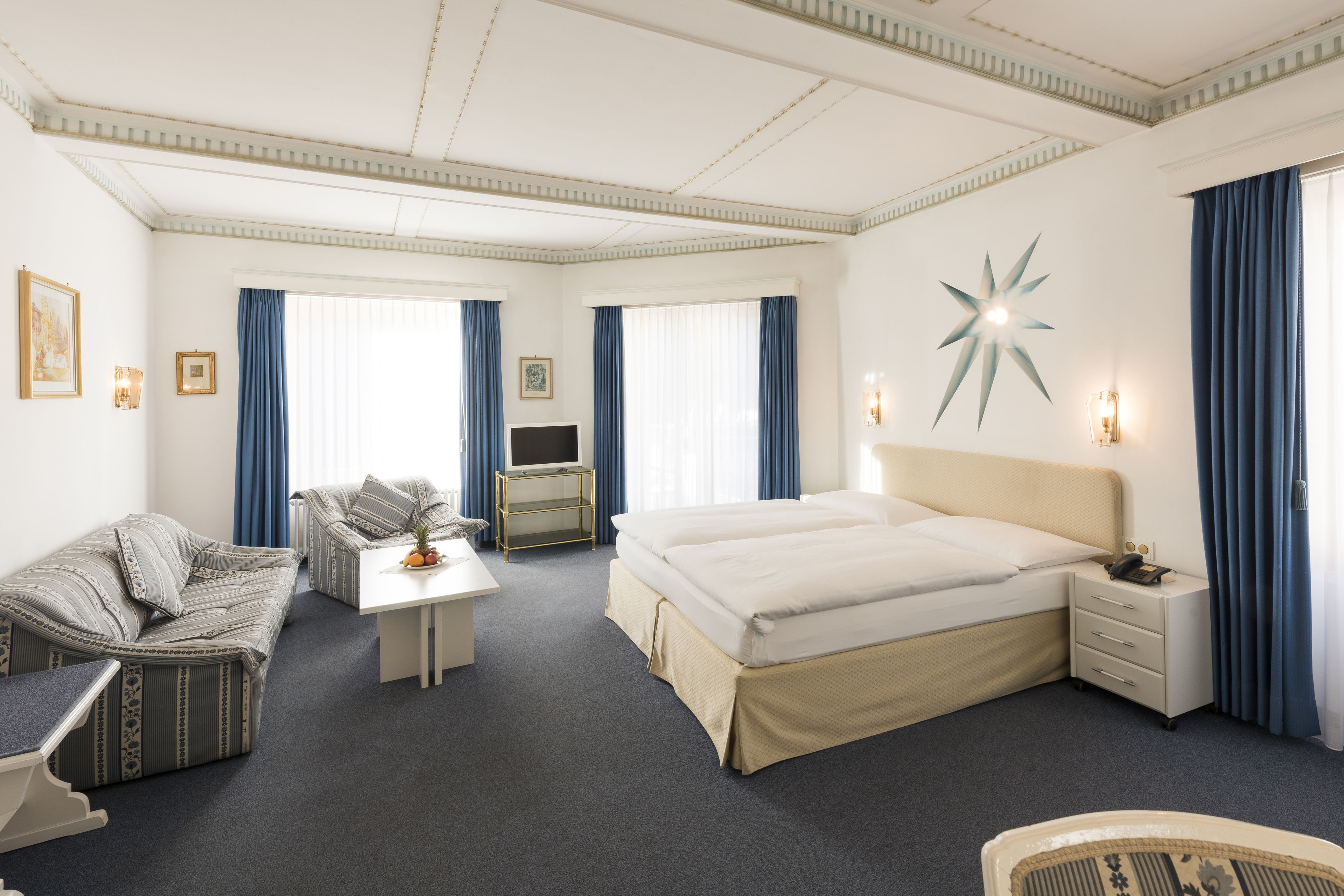 A hotel room with a large bed, a sofa, a desk, and a TV.